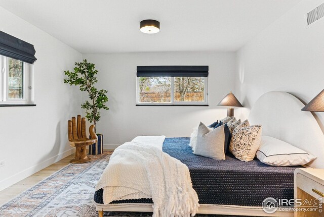 bedroom featuring baseboards, visible vents, wood finished floors, and multiple windows