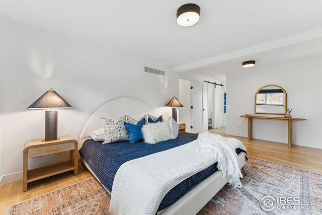 bedroom with wood finished floors, visible vents, baseboards, and a barn door