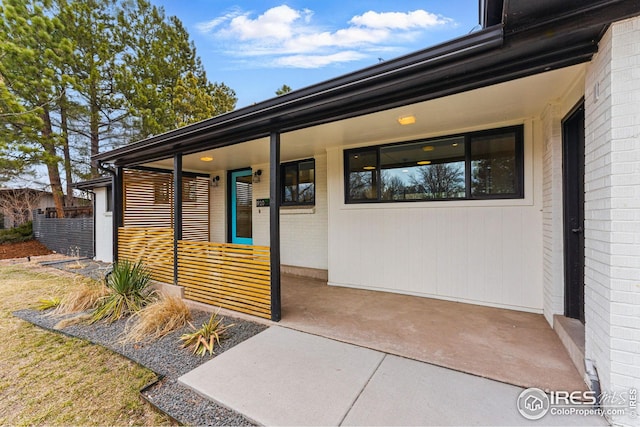 view of exterior entry featuring covered porch and brick siding