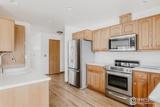 kitchen with a sink, stainless steel appliances, light wood-style floors, light brown cabinetry, and light countertops
