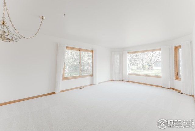 carpeted spare room featuring an inviting chandelier and baseboards