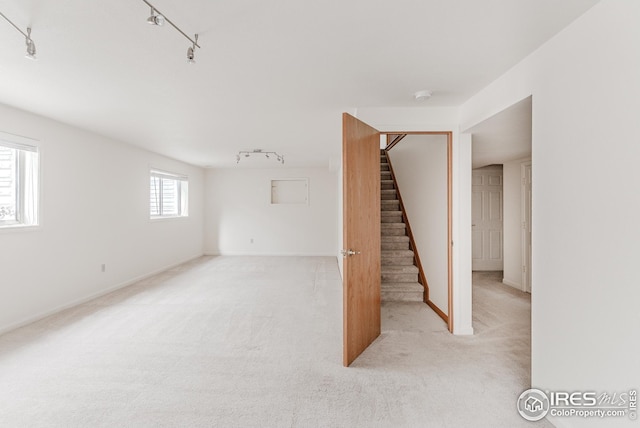 interior space with track lighting, stairway, light colored carpet, and baseboards