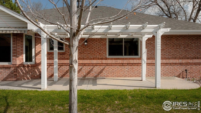 exterior space featuring a pergola, a patio area, a shingled roof, and brick siding