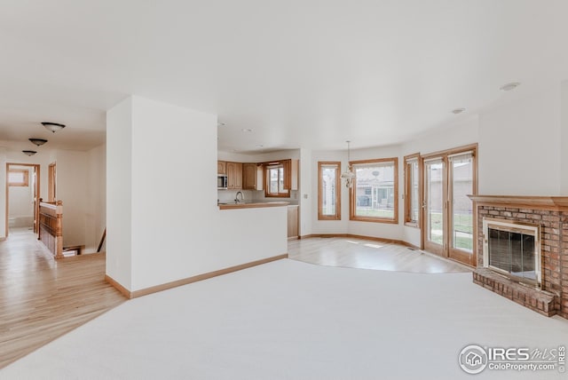 unfurnished living room featuring baseboards, light wood-style floors, a brick fireplace, and a sink