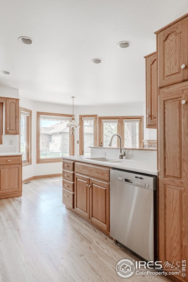kitchen with a sink, stainless steel dishwasher, light wood-style flooring, and light countertops