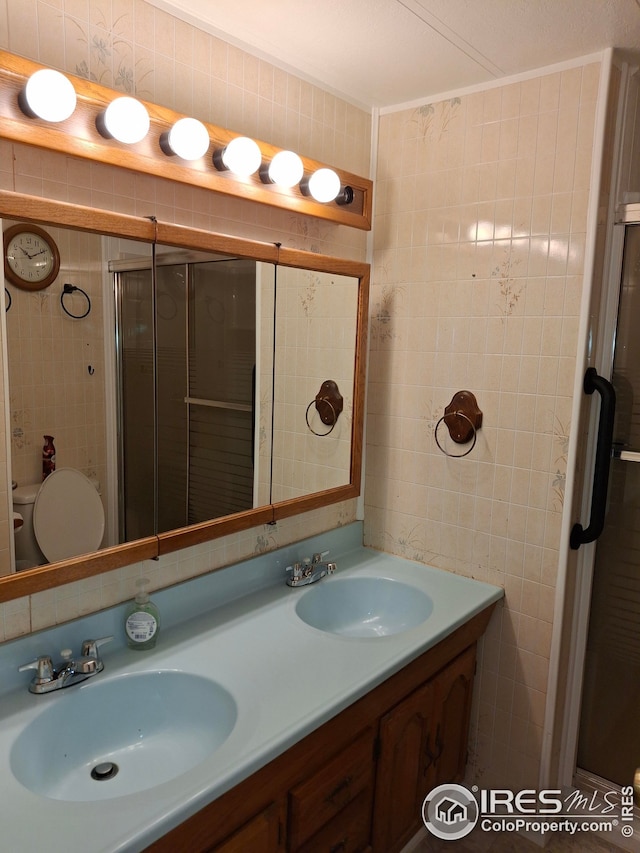 full bathroom with tile walls, a stall shower, double vanity, and a sink