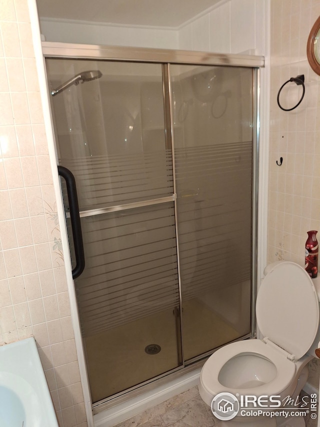 bathroom featuring toilet, a stall shower, and tile walls