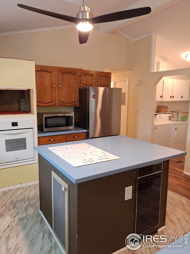 kitchen with appliances with stainless steel finishes, a kitchen island, separate washer and dryer, ornamental molding, and brown cabinetry