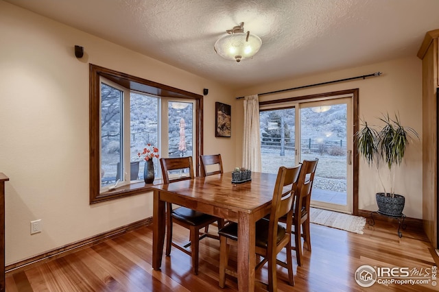 dining area featuring a textured ceiling, baseboards, and light wood-style flooring