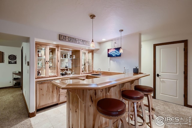 bar featuring indoor wet bar, baseboards, light colored carpet, a sink, and decorative light fixtures