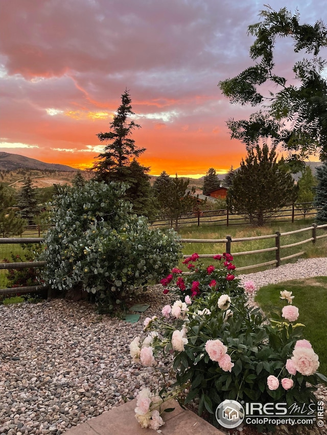 yard at dusk featuring a mountain view, fence, and a rural view