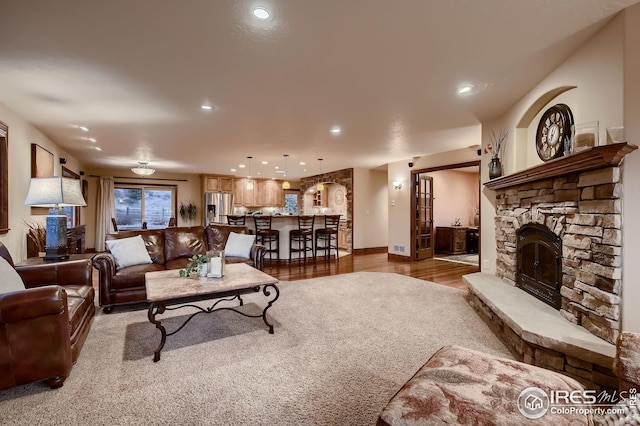 living area with baseboards, recessed lighting, a stone fireplace, and wood finished floors