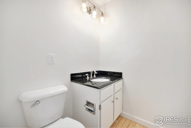 bathroom featuring toilet, baseboards, wood finished floors, and vanity