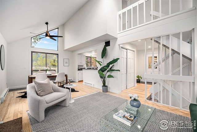 living room with ceiling fan, light wood finished floors, high vaulted ceiling, stairs, and baseboards