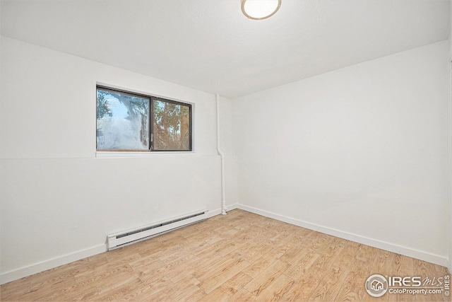 spare room featuring baseboards, a baseboard heating unit, and light wood finished floors