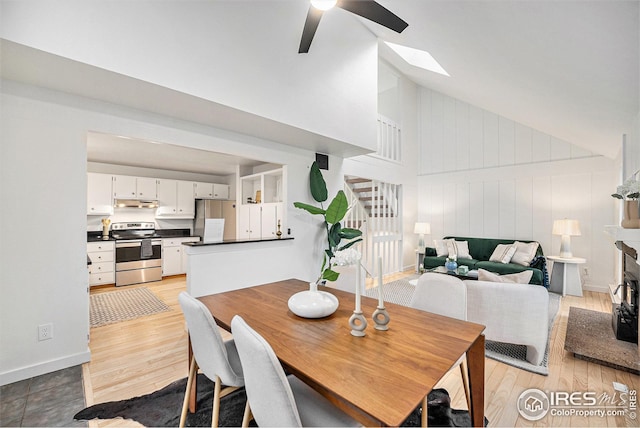 dining room with a skylight, high vaulted ceiling, light wood-style floors, and a ceiling fan