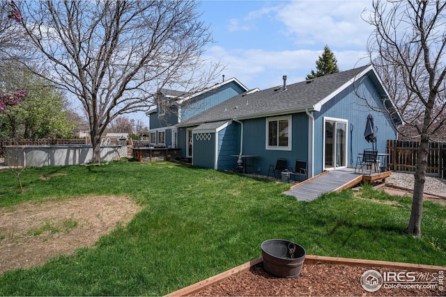 back of property with a lawn, a deck, fence, and a shingled roof