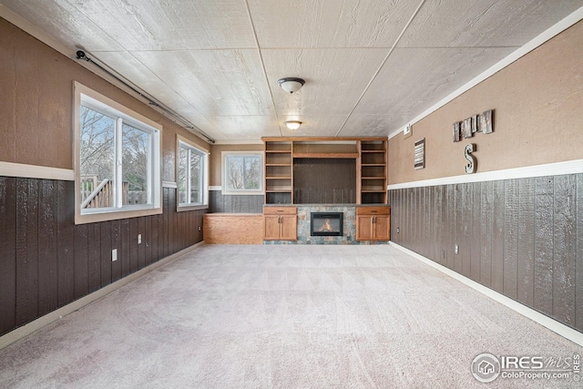 unfurnished living room featuring carpet floors, wainscoting, a glass covered fireplace, and wooden walls