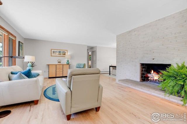 living area featuring a large fireplace, a baseboard radiator, and light wood-style flooring