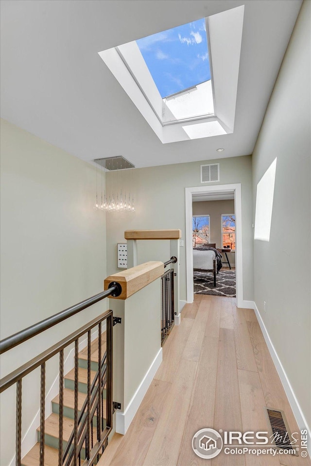 hallway featuring light wood finished floors, baseboards, an upstairs landing, a skylight, and visible vents