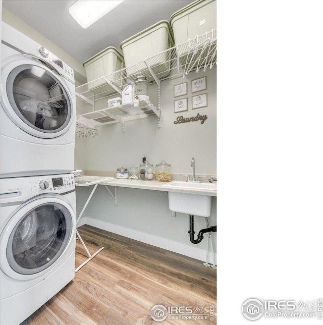 laundry room featuring laundry area, wood finished floors, stacked washing maching and dryer, baseboards, and a sink