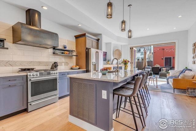 kitchen featuring light stone countertops, light wood-type flooring, island exhaust hood, appliances with stainless steel finishes, and backsplash