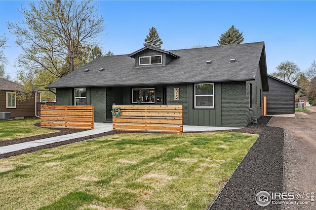view of front facade with roof with shingles, central air condition unit, board and batten siding, and a front lawn