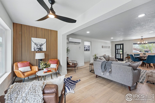 living room with a wall mounted AC, baseboards, ceiling fan with notable chandelier, light wood finished floors, and recessed lighting