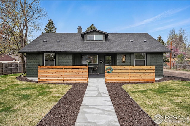 view of front of house with roof with shingles, a front lawn, brick siding, a chimney, and fence private yard