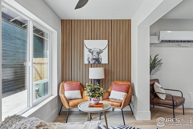 living area featuring wood finished floors, an accent wall, baseboards, ceiling fan, and a wall mounted AC