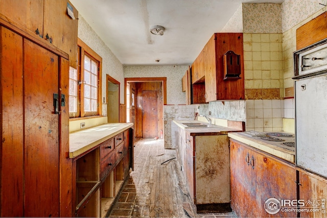 kitchen featuring brown cabinets, a sink, light countertops, hardwood / wood-style floors, and wallpapered walls