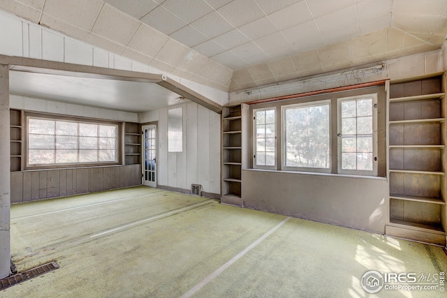 empty room with wooden walls, vaulted ceiling, a healthy amount of sunlight, and visible vents