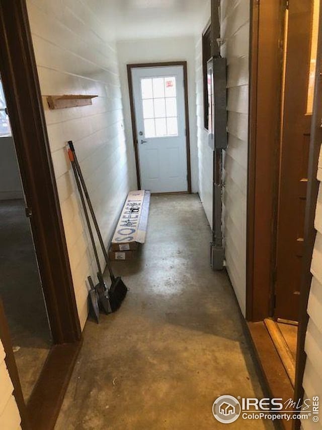 hall featuring unfinished concrete floors and tile walls