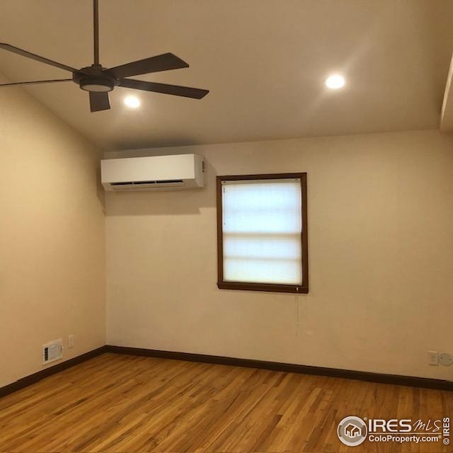empty room with a wall unit AC, a ceiling fan, visible vents, wood finished floors, and baseboards