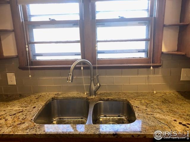 details featuring light stone counters, a sink, and tasteful backsplash