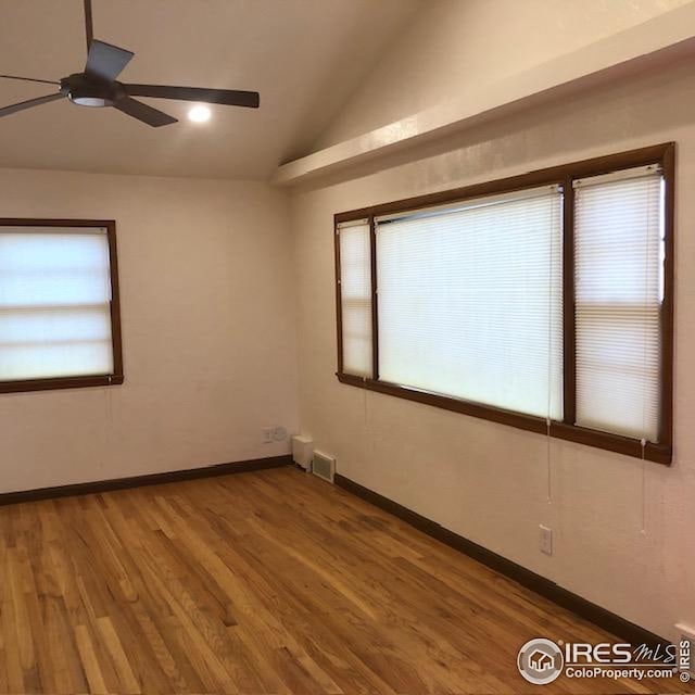 spare room with visible vents, lofted ceiling, wood finished floors, baseboards, and a ceiling fan