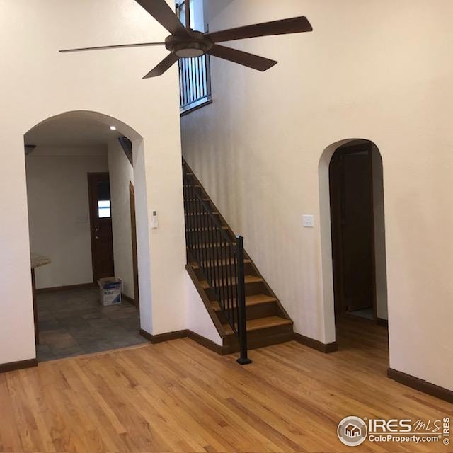 stairs featuring baseboards, arched walkways, ceiling fan, and wood finished floors