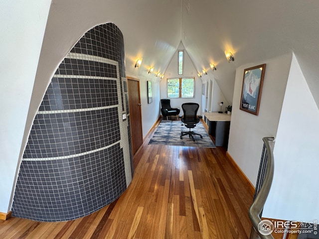 hallway featuring baseboards, wood finished floors, and lofted ceiling