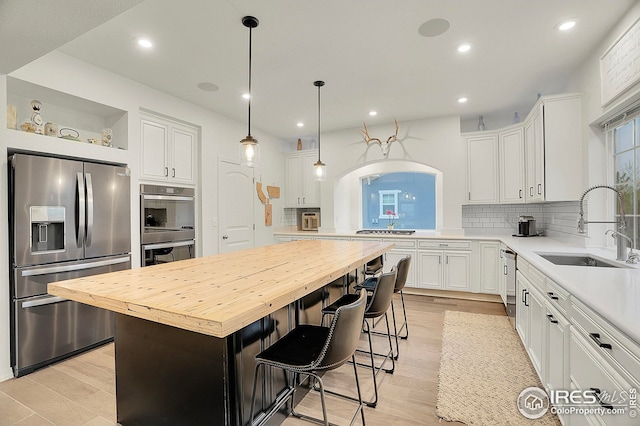 kitchen featuring backsplash, appliances with stainless steel finishes, a sink, butcher block counters, and white cabinetry