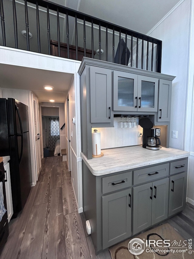kitchen featuring freestanding refrigerator, ornamental molding, glass insert cabinets, dark wood-style floors, and gray cabinetry