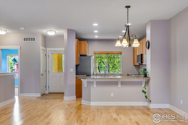 kitchen with visible vents, freestanding refrigerator, a kitchen bar, light wood-type flooring, and plenty of natural light