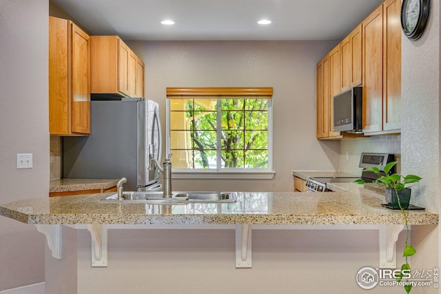 kitchen featuring a kitchen bar, recessed lighting, a sink, backsplash, and stainless steel appliances