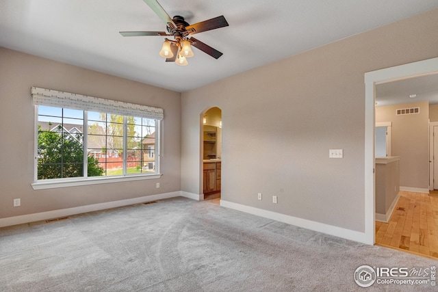 spare room featuring ceiling fan, light colored carpet, arched walkways, baseboards, and visible vents