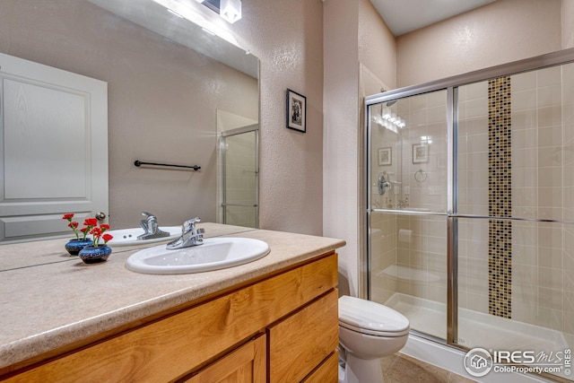 bathroom with vanity, a textured wall, a shower stall, and toilet
