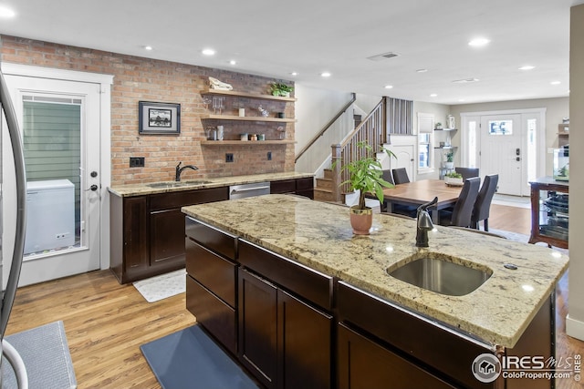 kitchen featuring a sink, a kitchen island with sink, light wood-style floors, and dishwasher