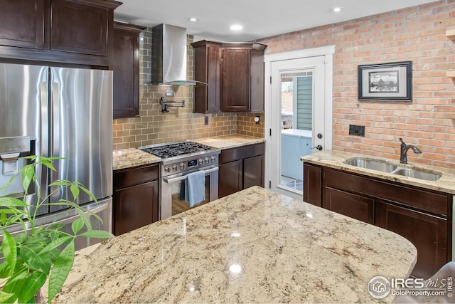 kitchen featuring wall chimney range hood, light stone countertops, a sink, washer / dryer, and stainless steel appliances
