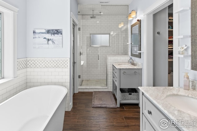 full bath with tile walls, a stall shower, wood finished floors, vanity, and a soaking tub
