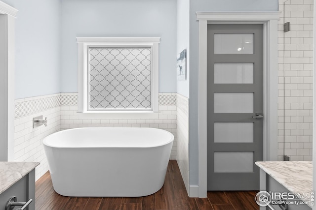 full bathroom with a freestanding tub, tile walls, a wainscoted wall, and vanity