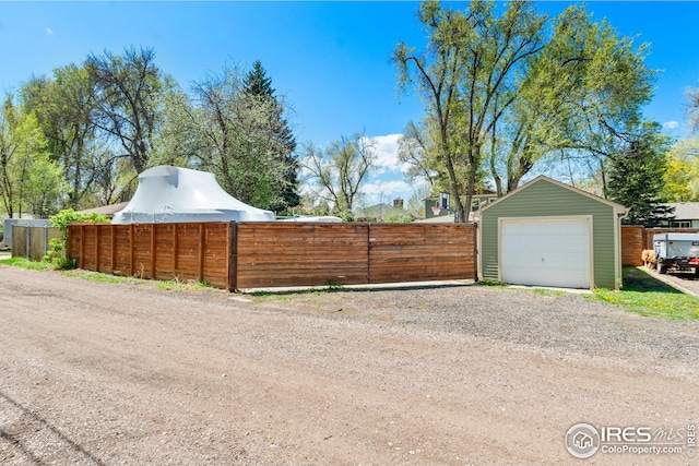 exterior space featuring a garage, fence, an outbuilding, and driveway