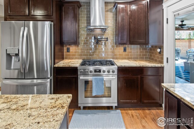 kitchen with dark brown cabinets, appliances with stainless steel finishes, decorative backsplash, and wall chimney exhaust hood
